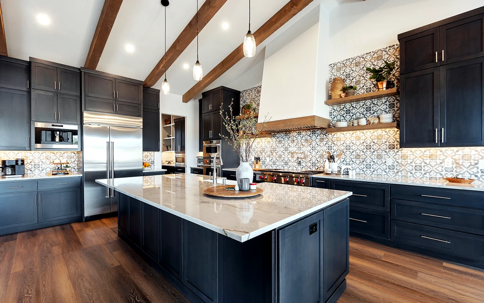 Custom kitchen cabinets with dark finish, patterned backsplash, island storage, and warm wood beams